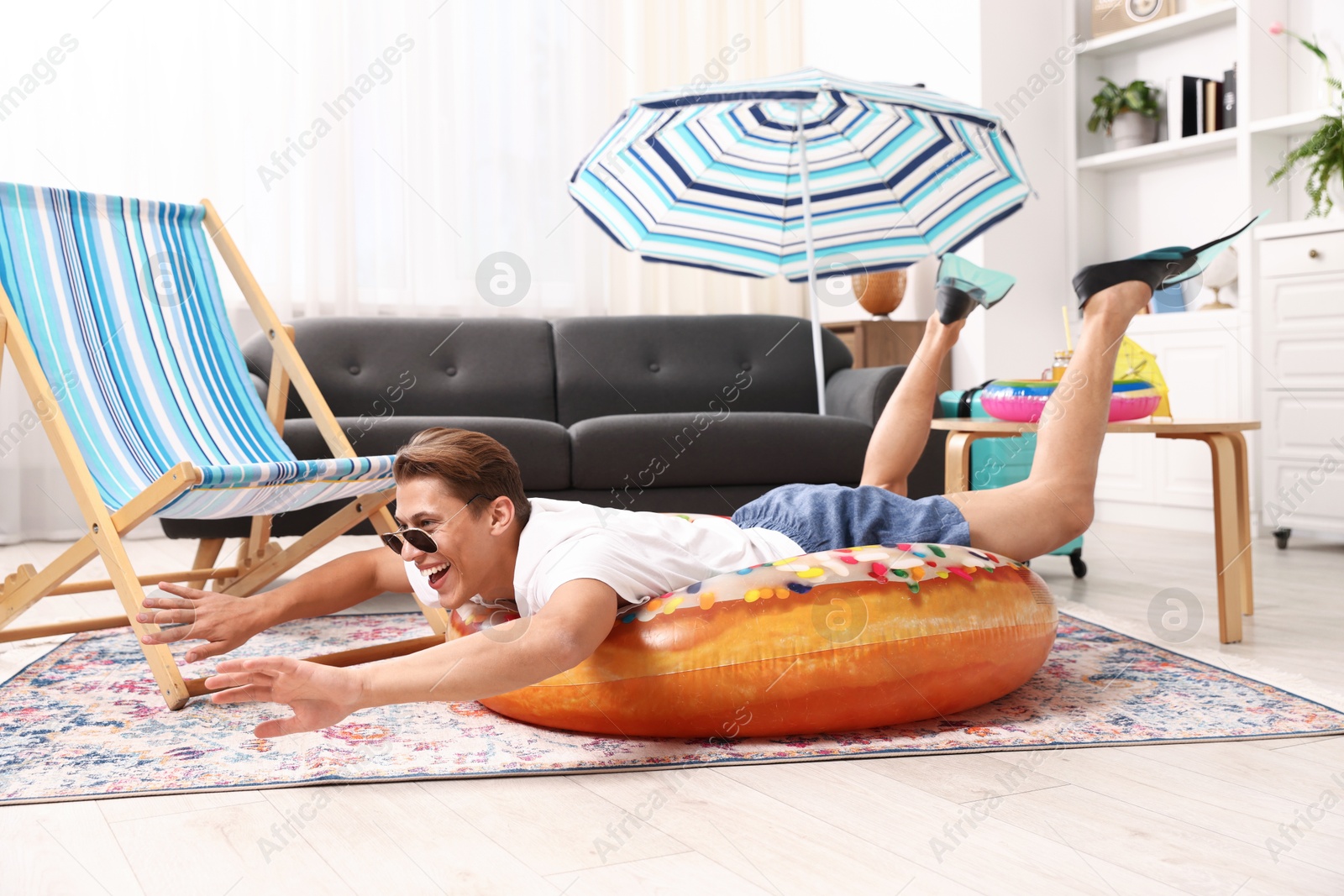 Happy man in sunglasses and flippers with inflatable ring having fun on floor at home. Dreaming about vacation at sea Photo of Happy man in sunglasses and flippers with inflatable ring having fun on floor at home. Dreaming about vacation at sea