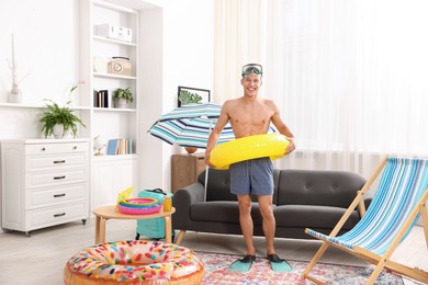 Photo of Happy man in flippers with diving mask and inflatable ring at home. Dreaming about vacation at sea