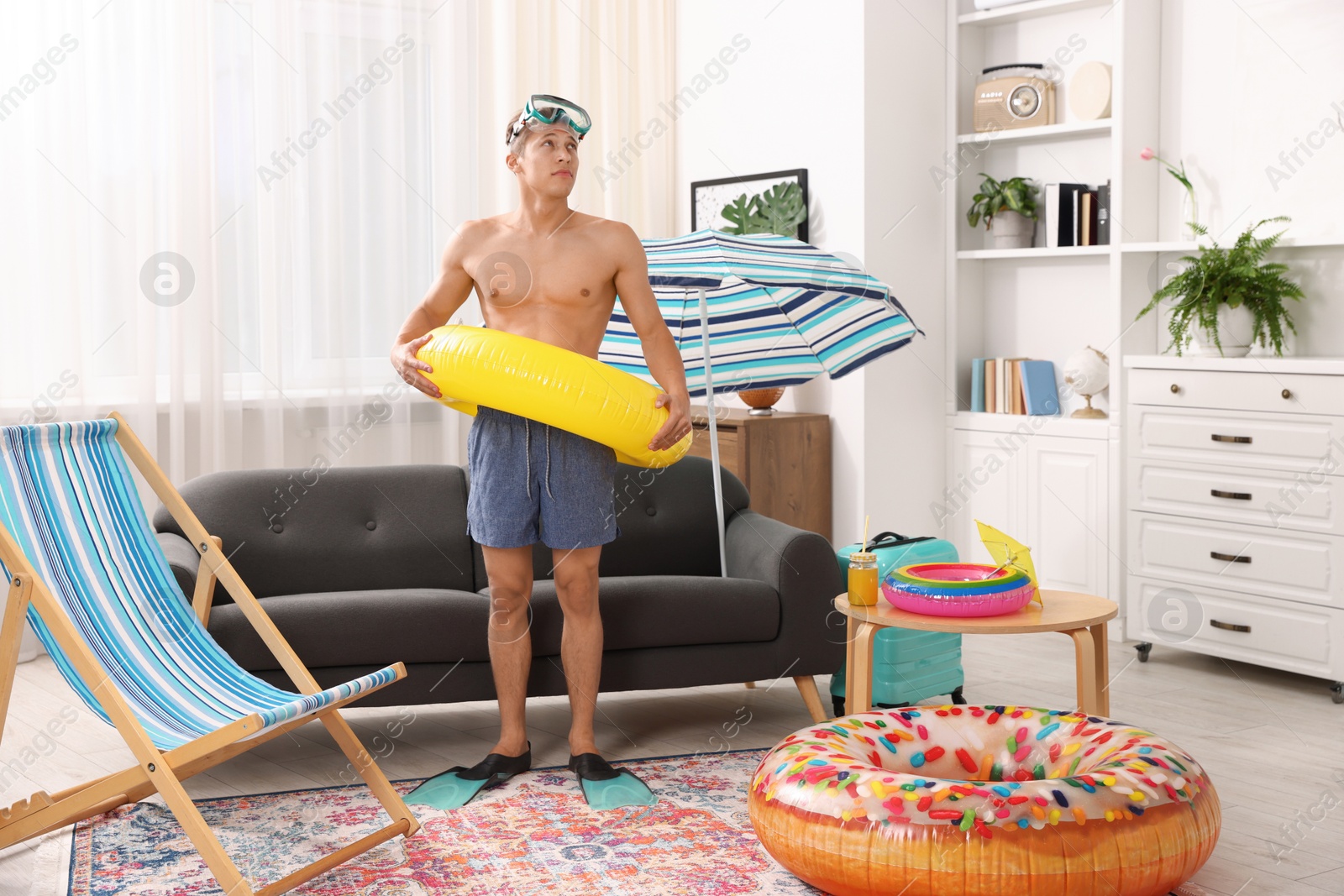 Man in flippers with diving mask and inflatable ring at home. Dreaming about vacation at sea Photo of Man in flippers with diving mask and inflatable ring at home. Dreaming about vacation at sea