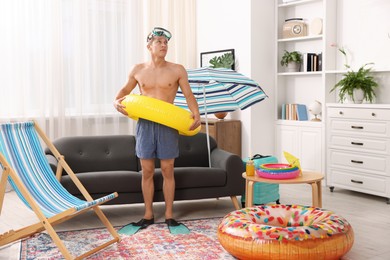 Photo of Man in flippers with diving mask and inflatable ring at home. Dreaming about vacation at sea