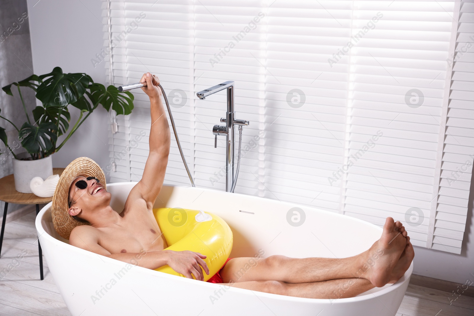 Happy man in sunglasses and straw hat with inflatable ring chilling in bathtub at home. Dreaming about vacation at sea Photo of Happy man in sunglasses and straw hat with inflatable ring chilling in bathtub at home. Dreaming about vacation at sea