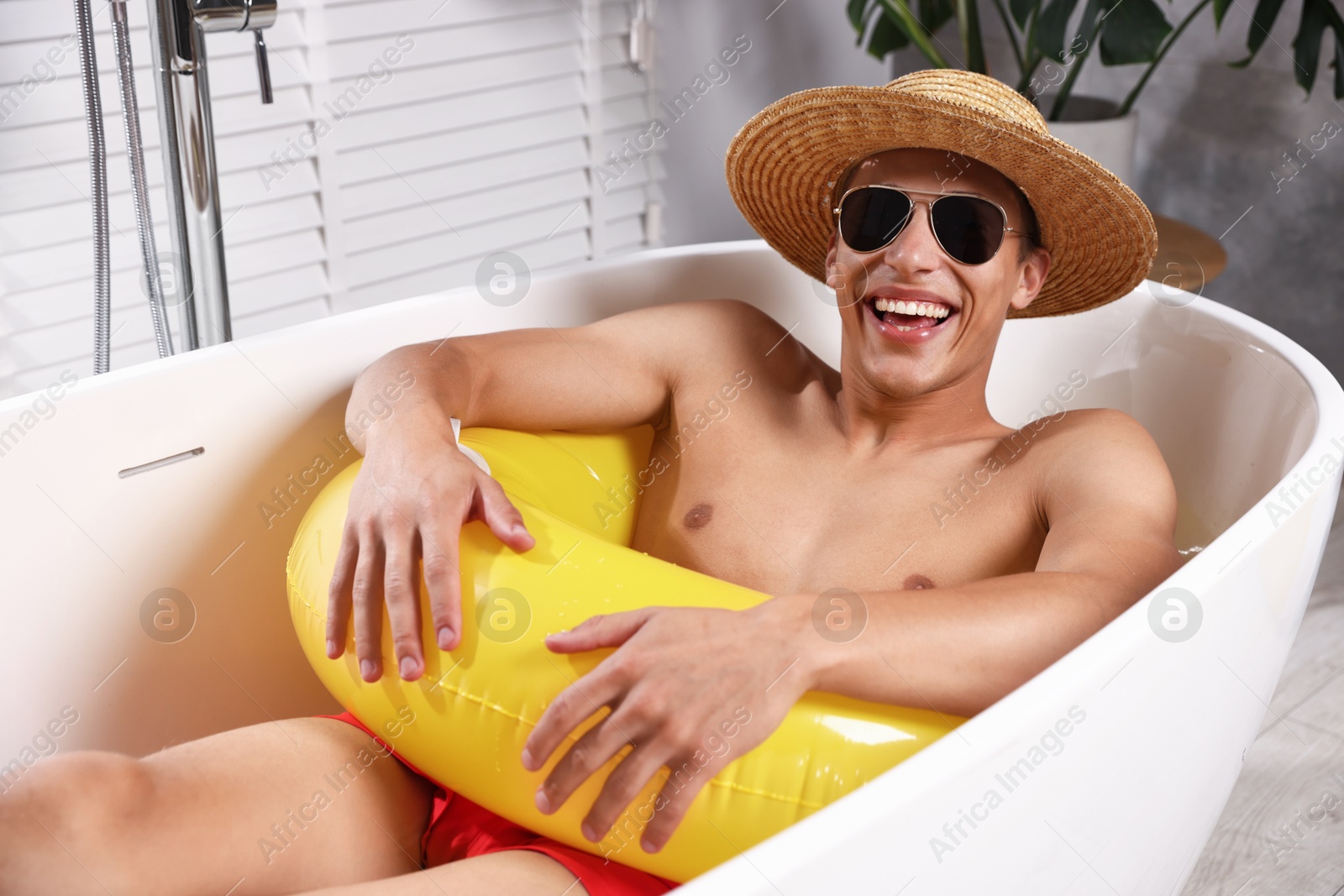 Happy man in sunglasses and straw hat with inflatable ring chilling in bathtub at home. Dreaming about vacation at sea Photo of Happy man in sunglasses and straw hat with inflatable ring chilling in bathtub at home. Dreaming about vacation at sea
