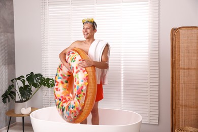 Photo of Happy man in with inflatable ring, diving mask and towel in bathtub at home. Dreaming about vacation at sea