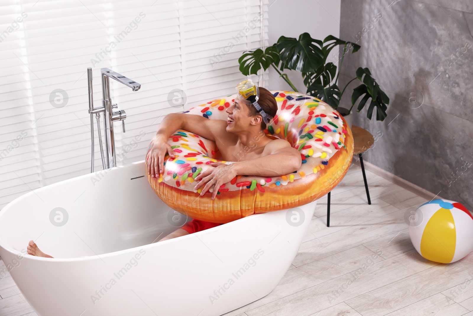 Happy man in with inflatable ring and diving mask chilling in bathtub at home. Dreaming about vacation at sea Photo of Happy man in with inflatable ring and diving mask chilling in bathtub at home. Dreaming about vacation at sea