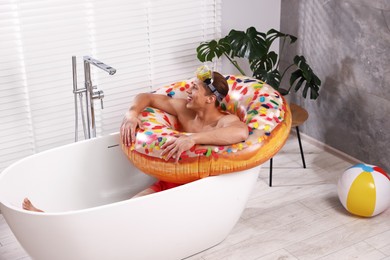 Photo of Happy man in with inflatable ring and diving mask chilling in bathtub at home. Dreaming about vacation at sea