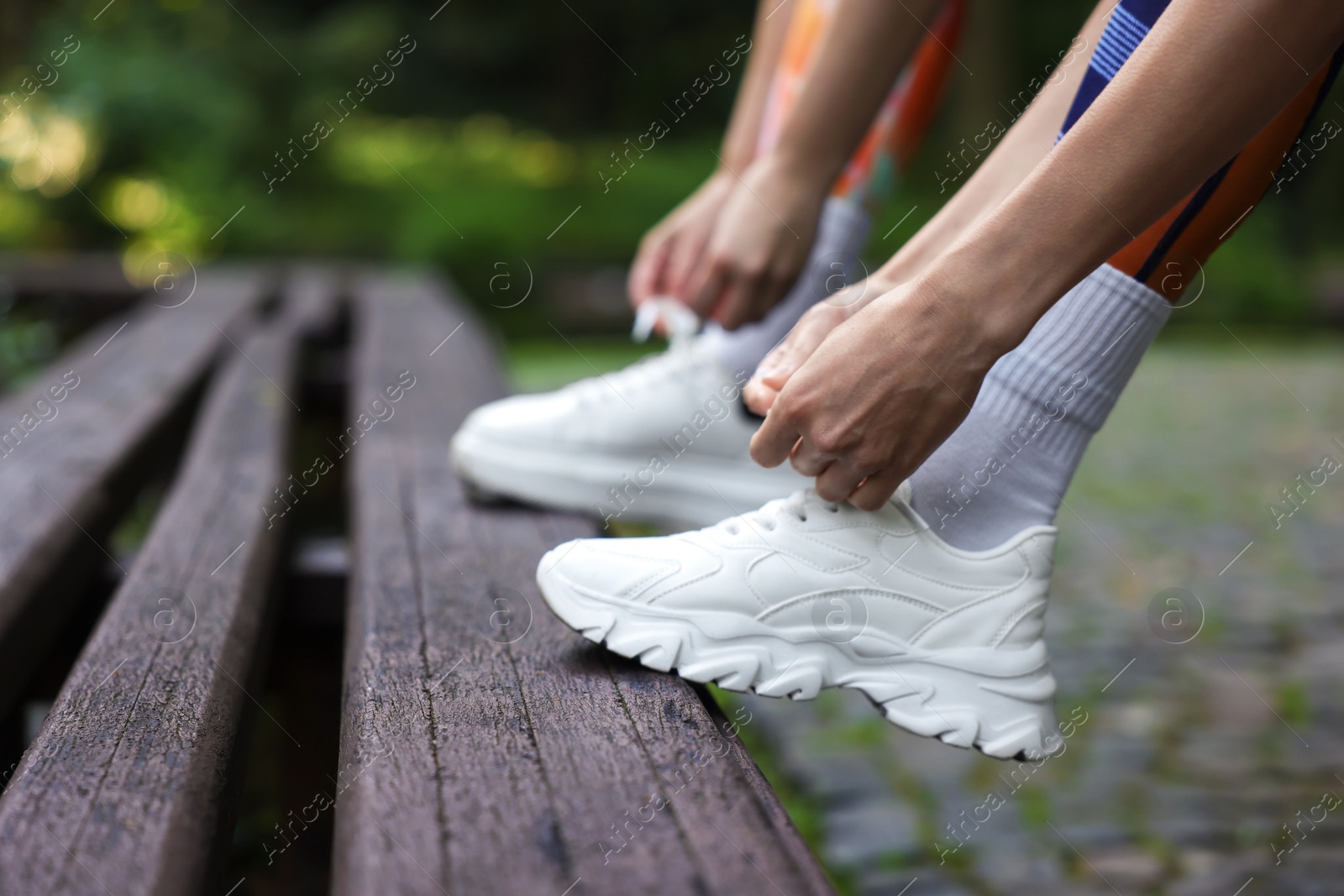 Photo of Woman and professional personal trainer tying shoes on wooden bench outdoors, closeup