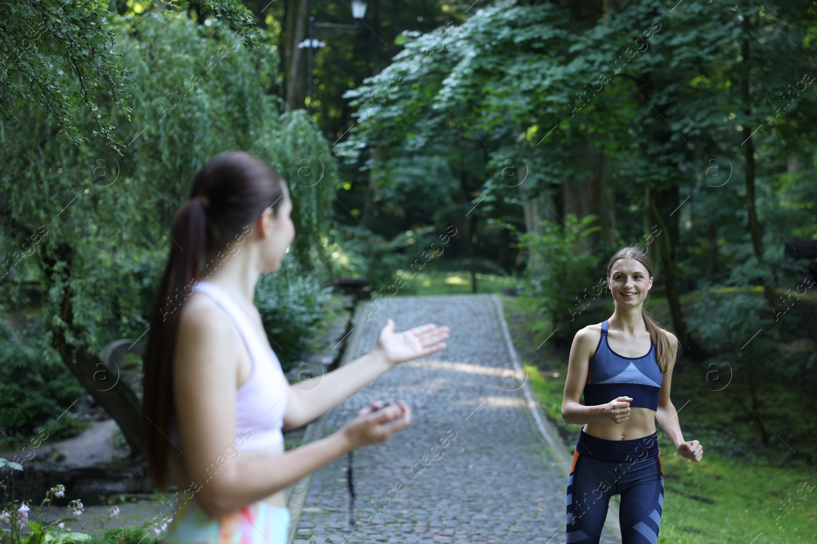 Photo of Young woman running with professional personal trainer outdoors, selective focus
