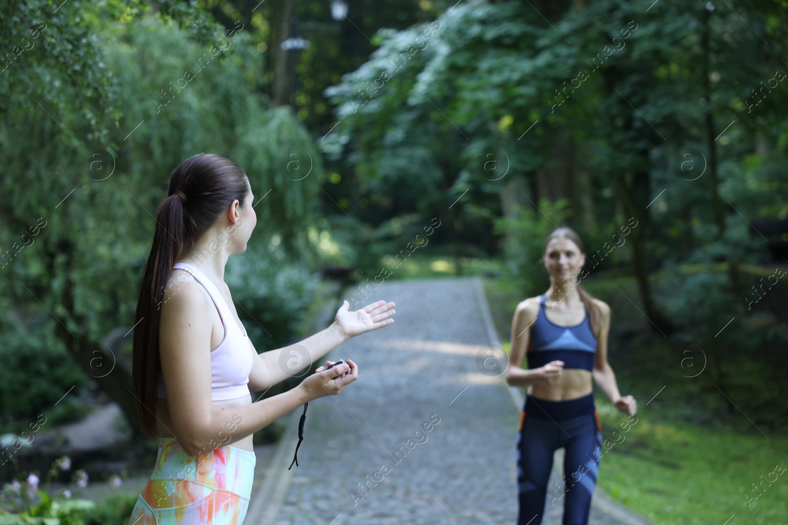 Photo of Young woman running with professional personal trainer outdoors, selective focus
