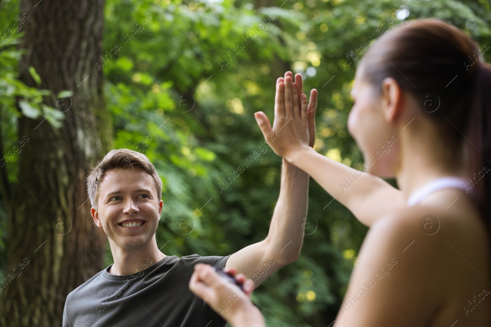 Photo of Young man with professional personal trainer giving high five outdoors, selective focus