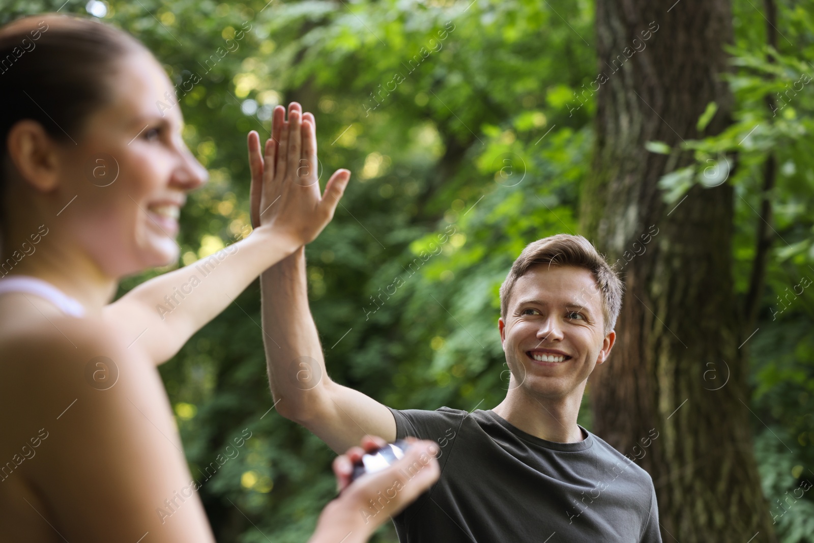 Photo of Young man with professional personal trainer giving high five outdoors, selective focus