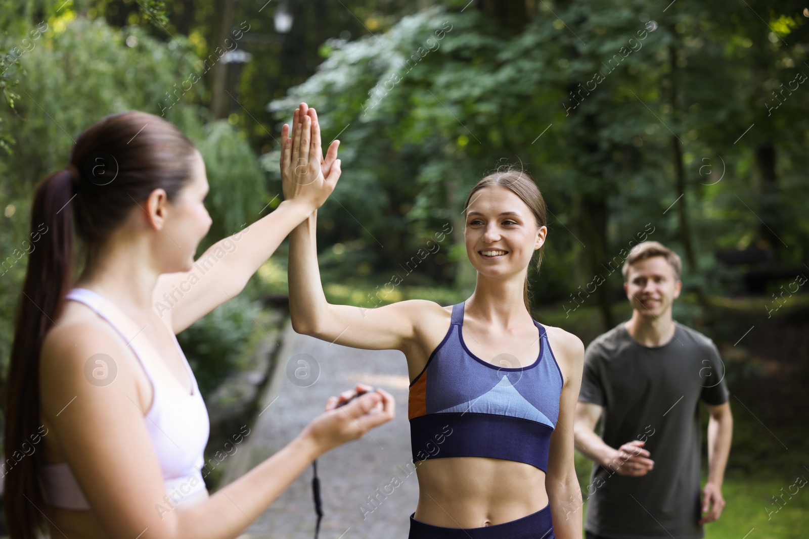 Photo of Young man and woman exercising with professional personal trainer and giving high five outdoors, selective focus