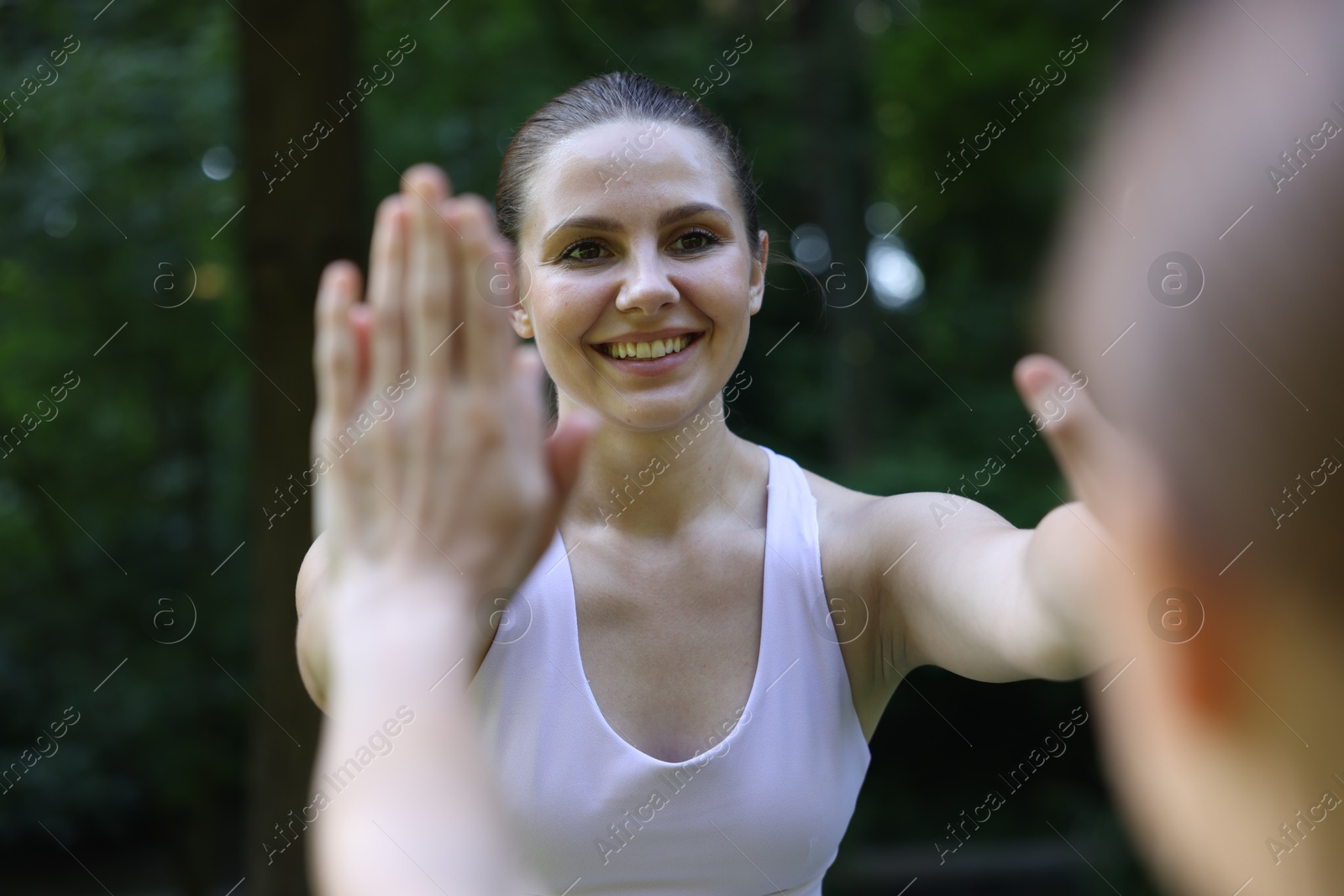 Photo of Young woman with professional personal trainer giving high five outdoors