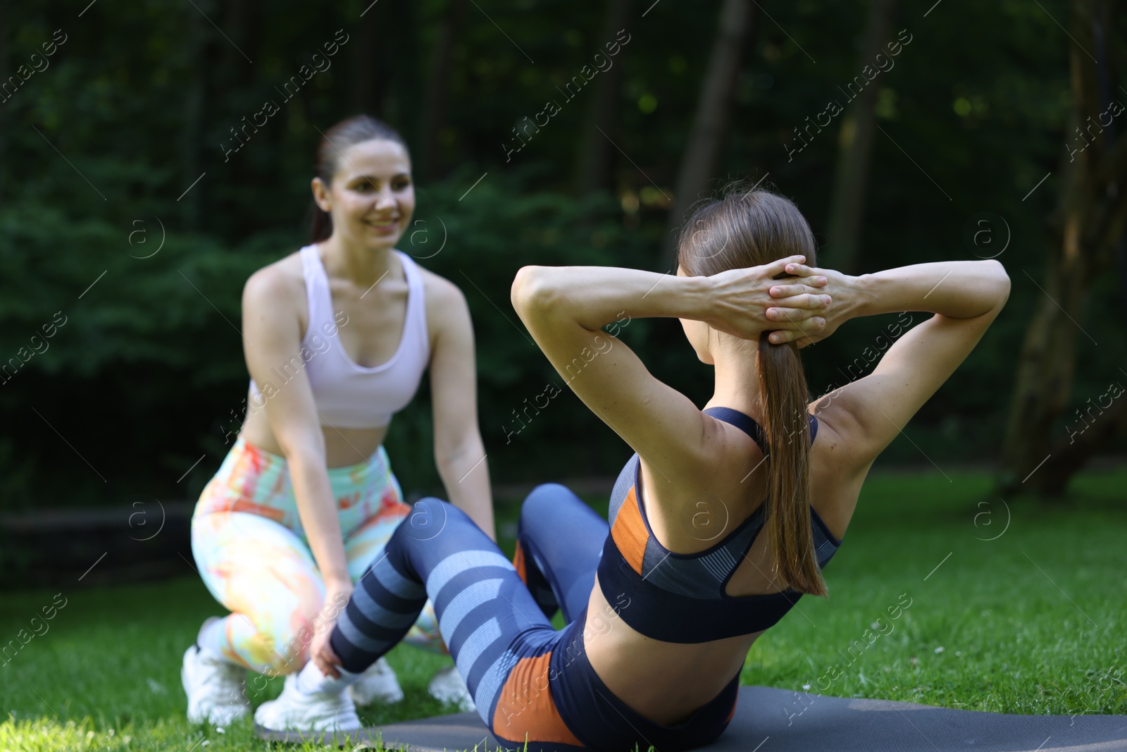 Photo of Young woman exercising with professional personal trainer outdoors, selective focus