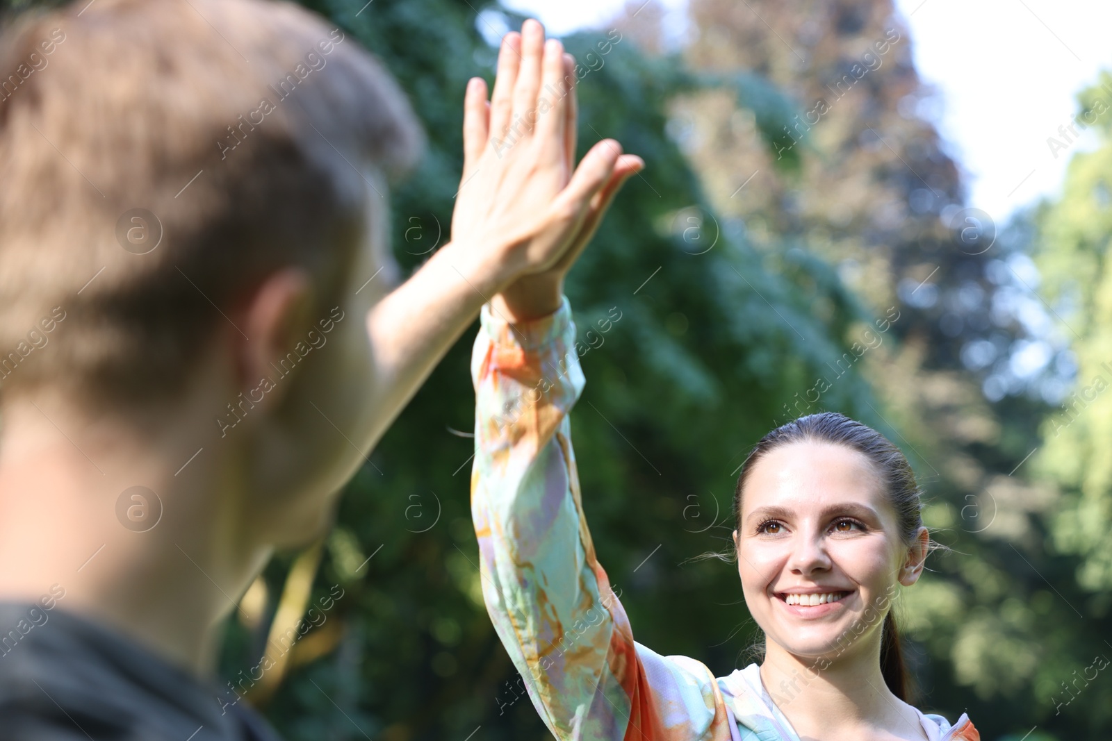 Photo of Young man with professional personal trainer giving high five outdoors