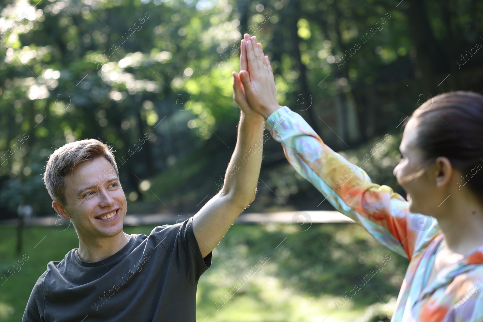 Photo of Young man with professional personal trainer giving high five outdoors