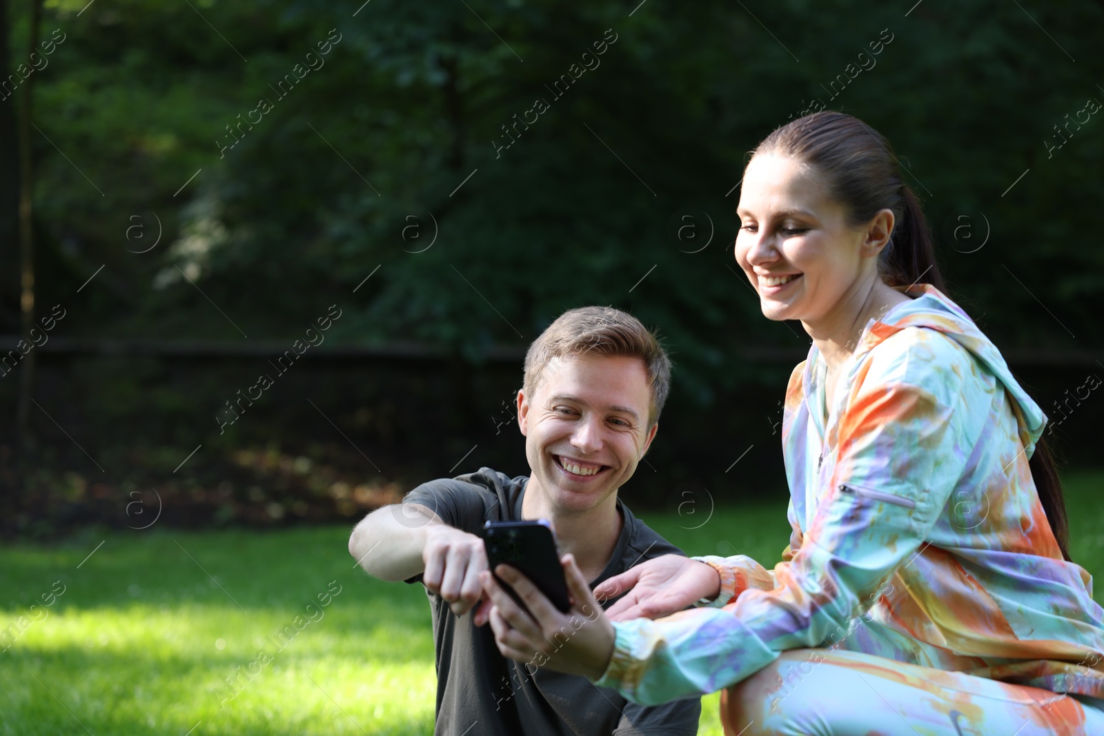 Photo of Young man with professional personal trainer looking at phone outdoors. Space for text