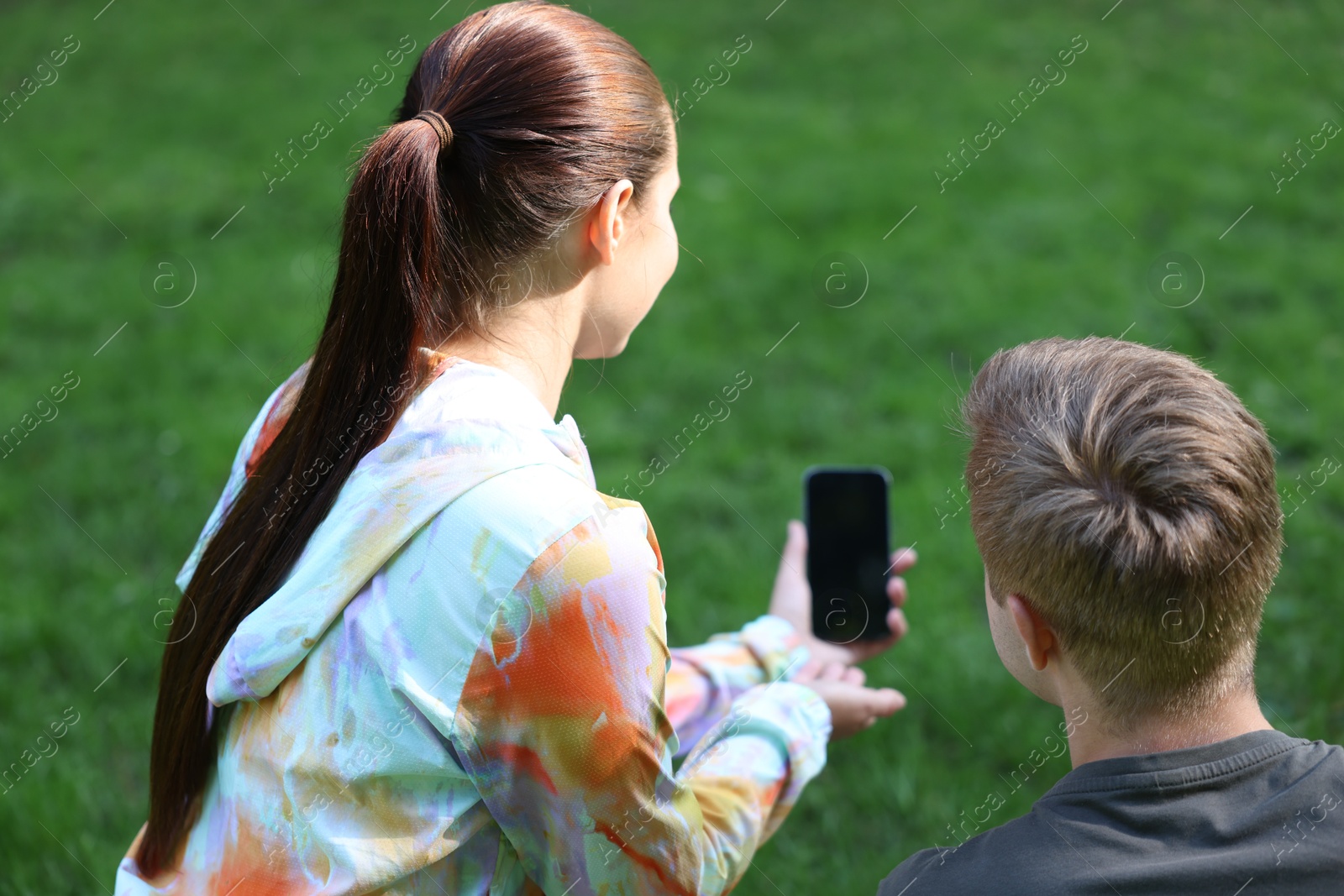 Photo of Young man with professional personal trainer looking at phone outdoors, back view