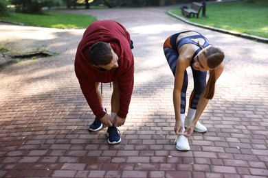 Photo of Young woman and professional personal trainer tying shoes outdoors