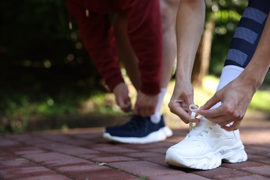 Photo of Young woman and professional personal trainer tying shoes outdoors, closeup