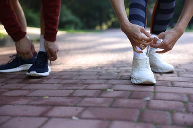 Photo of Young woman and professional personal trainer tying shoes outdoors, closeup