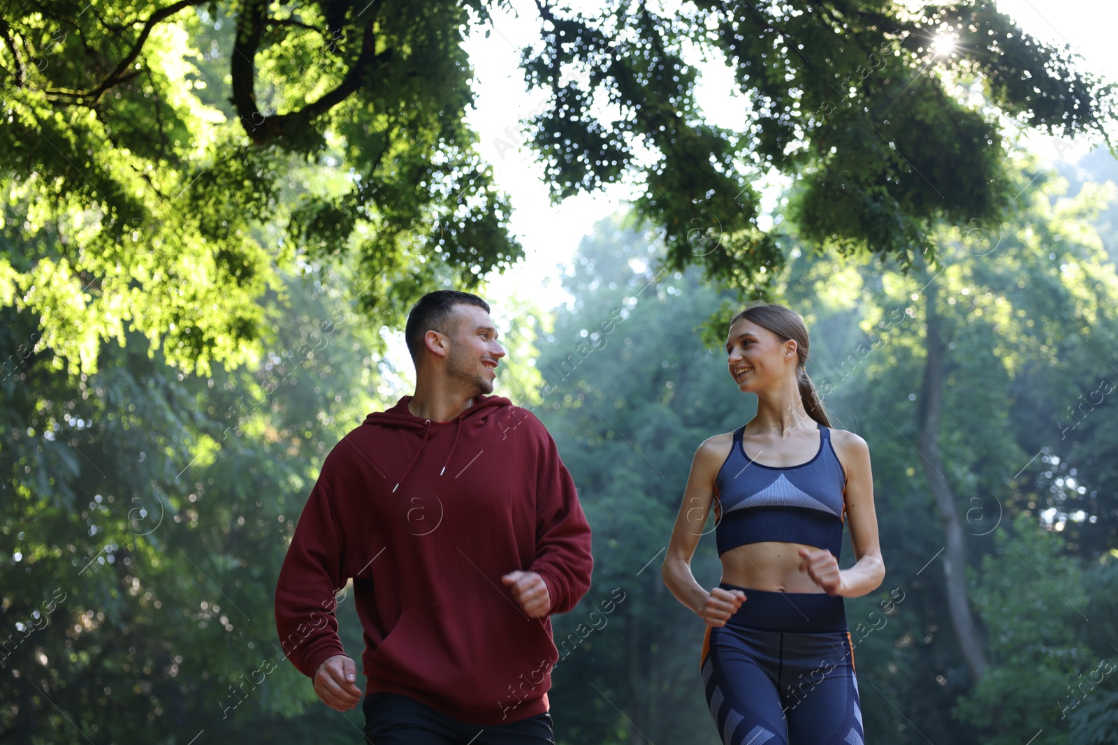 Photo of Young woman running with professional personal trainer outdoors, low angle view