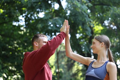 Photo of Young woman with professional personal trainer giving high five outdoors