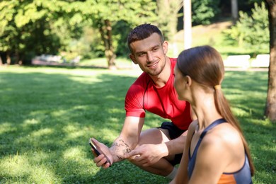 Photo of Young woman with professional personal trainer looking at smartphone outdoors. Space for text