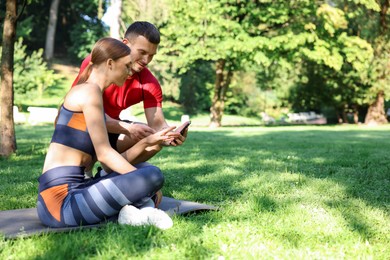 Photo of Young woman with professional personal trainer looking at smartphone outdoors. Space for text