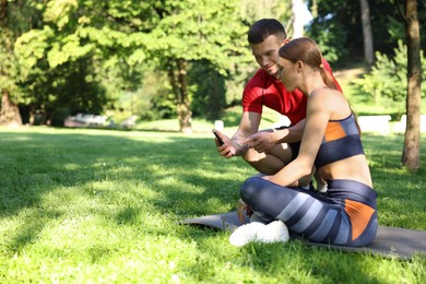 Photo of Young woman with professional personal trainer looking at smartphone outdoors. Space for text