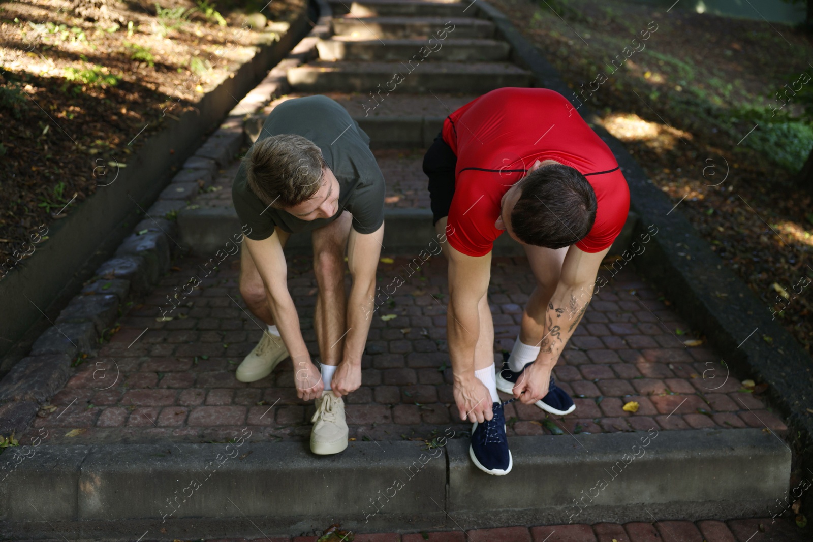Young man and professional personal trainer tying shoes outdoors Photo of Young man and professional personal trainer tying shoes outdoors