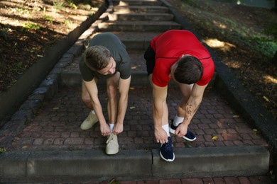 Photo of Young man and professional personal trainer tying shoes outdoors