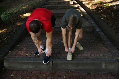 Photo of Young man and professional personal trainer tying shoes outdoors