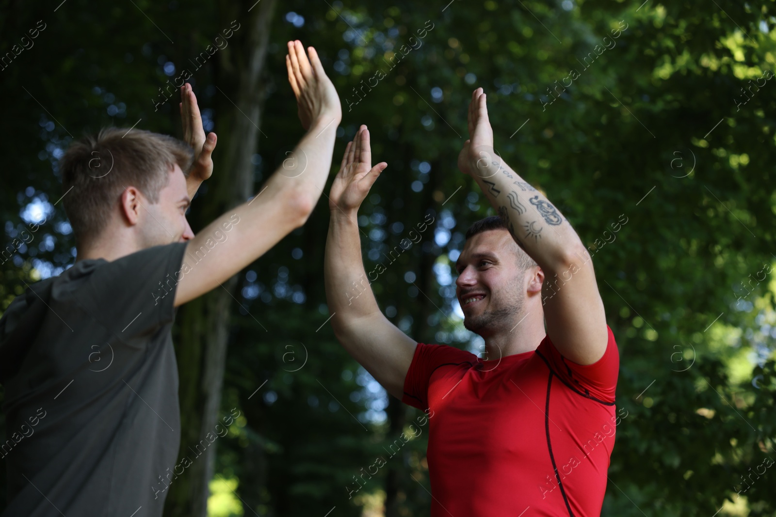 Photo of Young man with professional personal trainer giving high five outdoors