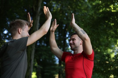 Photo of Young man with professional personal trainer giving high five outdoors