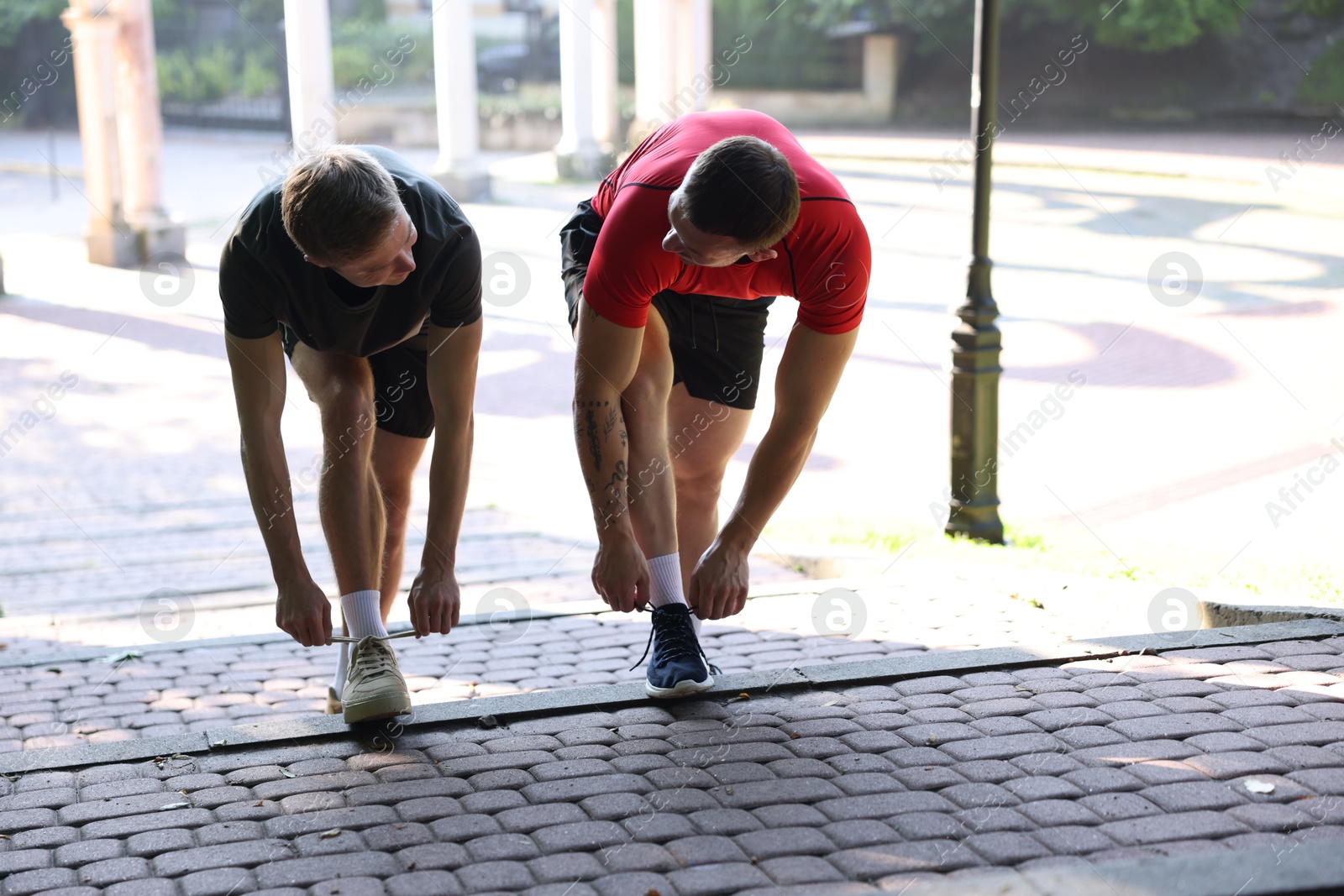 Photo of Young man and professional personal trainer tying shoes outdoors