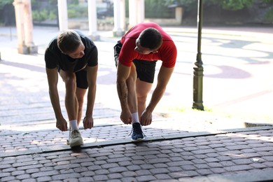 Photo of Young man and professional personal trainer tying shoes outdoors