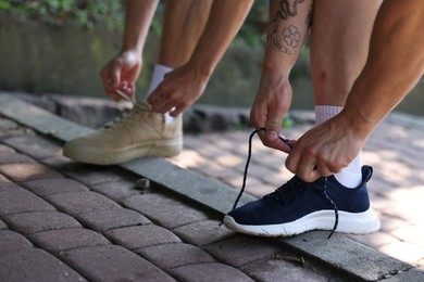 Photo of Young man and professional personal trainer tying shoes outdoors, closeup