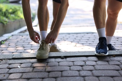 Photo of Young man and professional personal trainer tying shoes outdoors, closeup