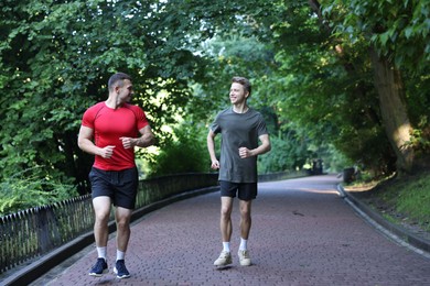 Photo of Young man running with professional personal trainer outdoors. Space for text