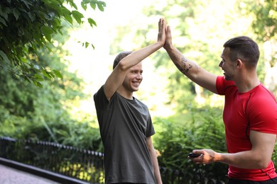 Photo of Young man with professional personal trainer giving high five outdoors