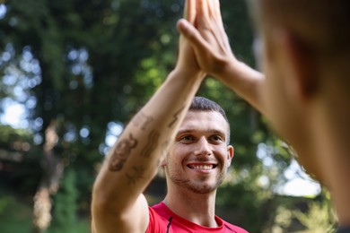 Photo of Young man with professional personal trainer giving high five outdoors