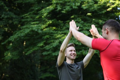 Photo of Young man with professional personal trainer giving high five outdoors. Space for text