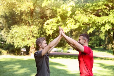 Photo of Young man with professional personal trainer giving high five outdoors
