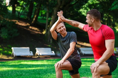 Photo of Young man with professional personal trainer giving high five outdoors