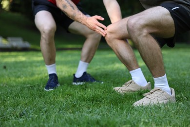 Photo of Young man exercising with professional personal trainer outdoors, closeup