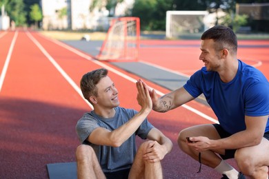 Photo of Young man with professional personal trainer giving high five outdoors