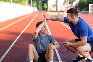 Photo of Young man with professional personal trainer giving high five outdoors