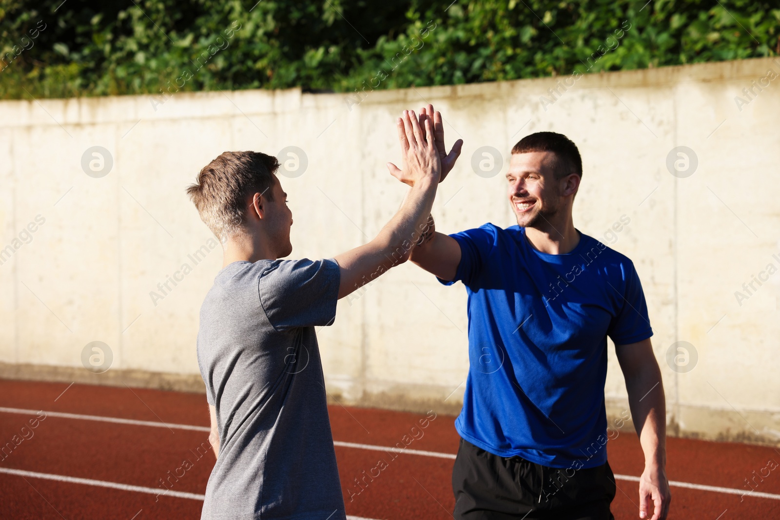 Young man with professional personal trainer giving high five outdoors Photo of Young man with professional personal trainer giving high five outdoors