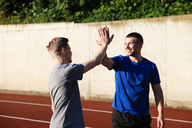 Photo of Young man with professional personal trainer giving high five outdoors