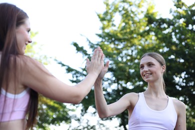 Photo of Young woman with professional personal trainer giving high five outdoors, selective focus